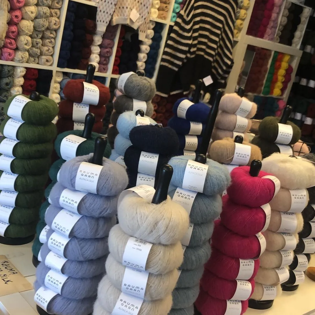 Garnnøster stablet på pinner foran fulle garnhyller i butikken